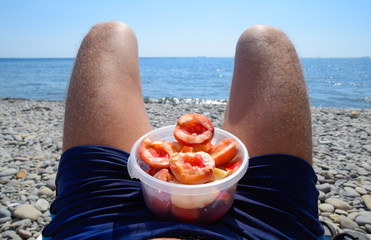 Peaches on the knees. Peeled peaches in a cup on male hairy legs. Beach vacation by the sea.