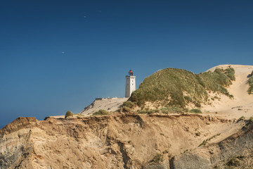 Beautiful cliff beach sand dunes and landmark lighthouse landscape scene with blue sky. Rubjerg Knude Lighthouse, L&oslash;nstrup in North Jutland in Denmark, Skagerrak, North Sea