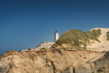 Beautiful cliff beach sand dunes and landmark lighthouse landscape scene with blue sky. Rubjerg Knude Lighthouse, Lønstrup in North Jutland in Denmark, Skagerrak, North Sea
