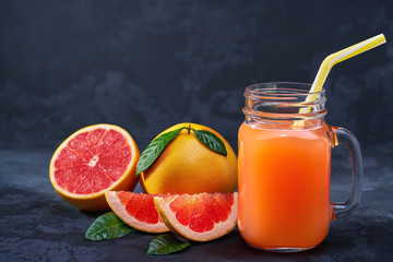 Naklejka na ściany i meble Glass jar of fresh grapefruit juice with fresh fruits on dark table.