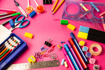 Felt pens, pencils, clips of different colors on a pink background