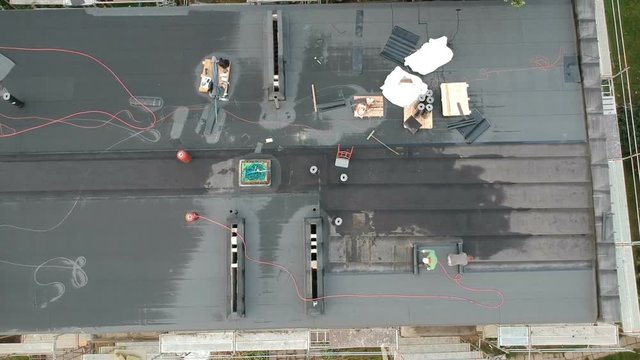 Two workers repair waterproofing apartment flat house roof, aerial view
