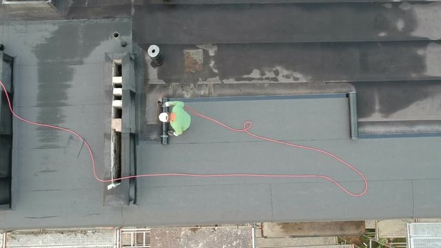 Worker on flat roof fixing waterproofing material, aerial view

