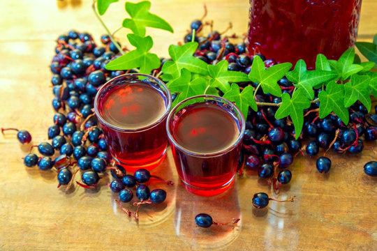 Homemade liquor in shot glasses with black current berries on the table. Fruit flavor alcohol drink with natural ingredients concept.