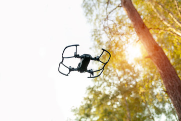 Small Smart Drone quadrocopter Flying on White Sky and Green trees.