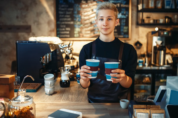 Male barista holds two cups of fresh hot coffee
