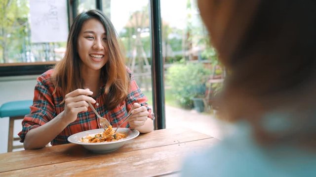Beautiful happy Asian women lesbian lgbt couple sitting each side eating a plate of Italian seafood spaghetti and french fries at restaurant or cafe while smiling and looking at food.