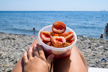 Peeled peaches in a cup on female legs. Beach vacation by the sea.