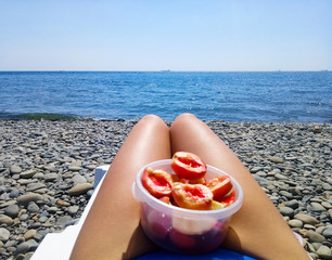 Peeled peaches in a cup on female legs. Beach vacation by the sea.