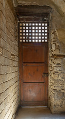 Fototapeta na wymiar Facade of old abandoned stone bricks wall with one weathered wooden door and wooden grid window, Old Cairo, Egypt