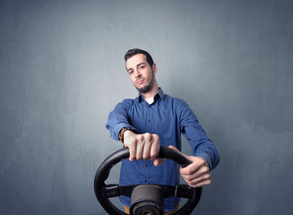 Fototapeta na wymiar Young man holding black steering wheel on a blueish gray background
