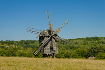 Plakat Antique old wooden windmill under blue sky in front of forest. Sunny summer day. National Museum of Folk Architecture and Life of Ukraine in Pyrohiv. 
