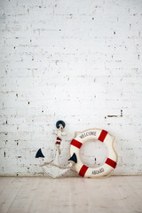 A composition on a sea theme with an anchor and life ring on a white brick wall.
