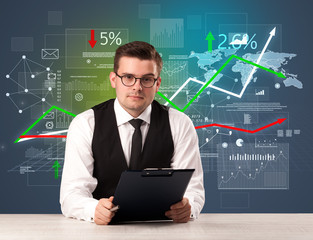 Young handsome businessman sitting at a desk with stocks and progress charts behind him