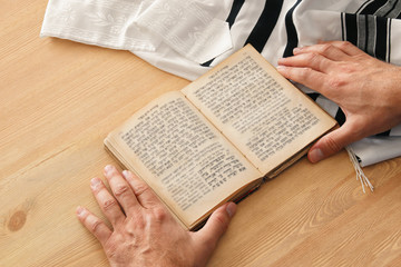 Jewish man hands holding a Prayer book, praying, next to tallit. Jewish traditional symbols. Rosh...