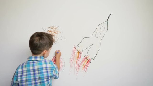 little child drawing thr rocket on white wall