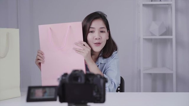 Happy beautiful Asian woman unboxing gifts from brand or her subscribers. Female blogger recording video from camera to fliming an unboxing video.