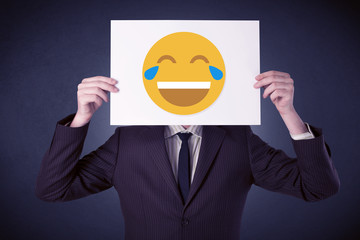 Young businessman hiding behind a laughing emoticon on cardboard