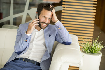 Happy young businessman sitting in office and using mobile phone