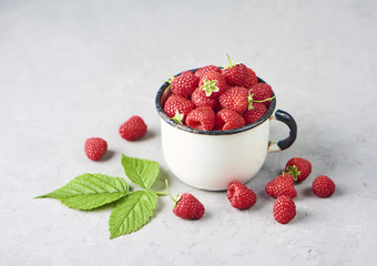 Fresh and ripe raspberry in mug, green leaves