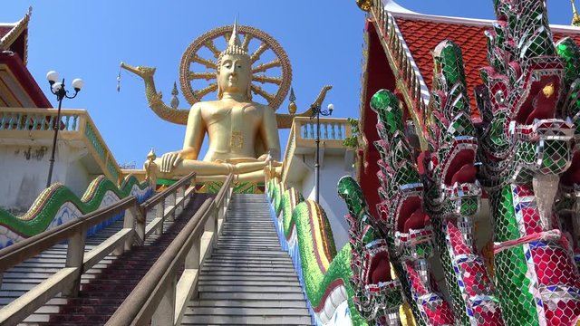 Panorama of stairs decorated by seven-headed Naga or Mucalinda and leading to golden statue of Big Buddha sitting against wheel of Dharma on background. Wat Phra Yai temple, Koh Samui, Thailand.