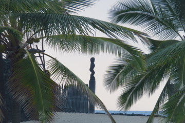 Silhouette  of a Tiki woman statue surrounded by palm trees in the evening light at Puuhonua o...