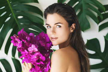 Young and beautiful woman with perfect smooth skin is holding orchid flowers
