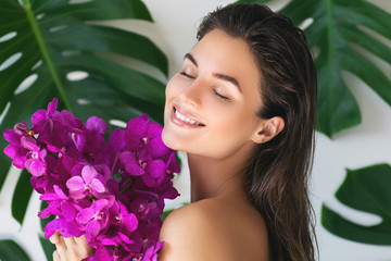 Young and beautiful woman with perfect smooth skin is holding orchid flowers
