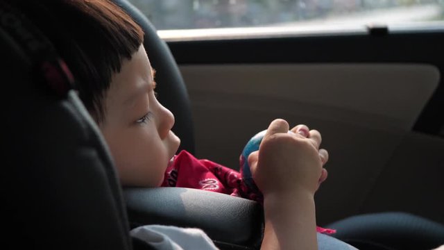 cute child sitting on car seat, hand playing small ball