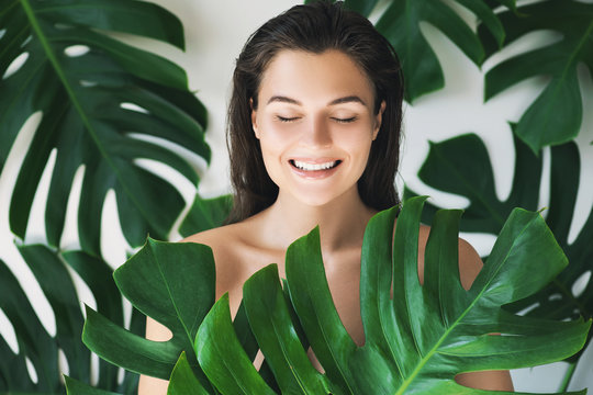 Portrait of young and beautiful woman with perfect smooth skin in tropical leaves