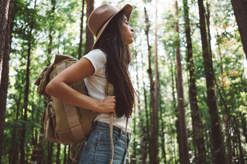 Pensive brave woman with backpack traveling alone among trees in forest on outdoors.