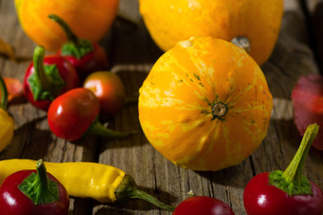 red cherry peppers, yellow chili and pumpkins on old wood table