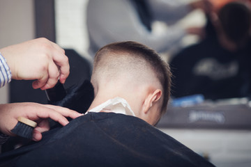 Back view of cute boy getting hairstyle by hairdresser in barbershop.
