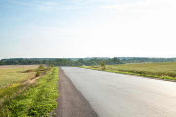 Asphalt road through the fields at sunset