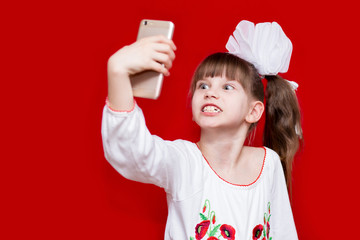 Little girl with crazy face hold telephone and take picture on red background. Communication concept