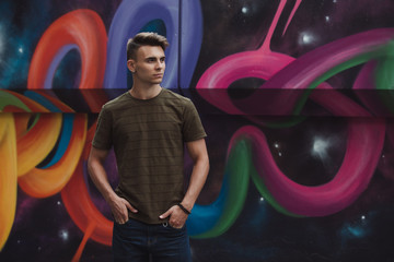 Handsome man model in khaki color polo posing against street art wall