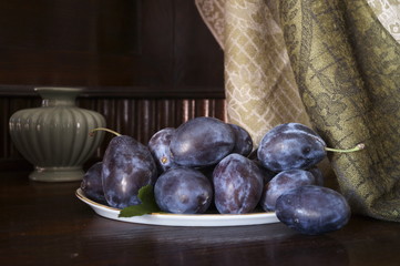 Rustic background with plums plate, gas lamp and vase flower
