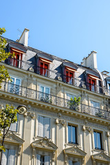 View from down the street of a typical parisian, opulent-looking building of haussmannian style with cut stone facade, carved ornaments, balcony and orange awnings on the top floor windows.