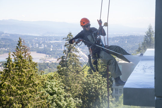 High rise rope access window cleaner is power washing the building during a hot sunny summer day. Taken in Burnaby Mountain, Vancouver, BC, Canada.