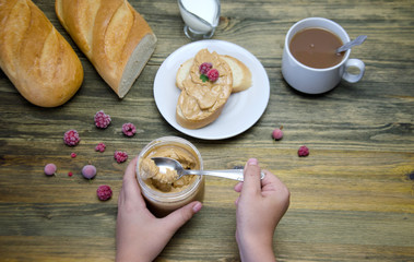 a loaf of bread and a sandwich a piece of loaf with nut paste a Cup and children's hands holding a jar with nut paste and berry