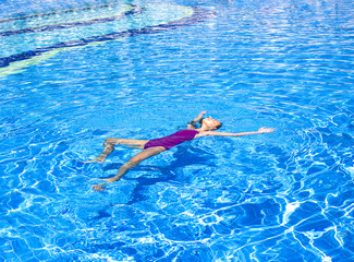 Slender teenage girl swims on her back in the outdoor pool