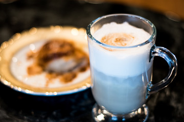 Cappuccino In Glass Mug With Croissant In Background On Dark Table At Diner