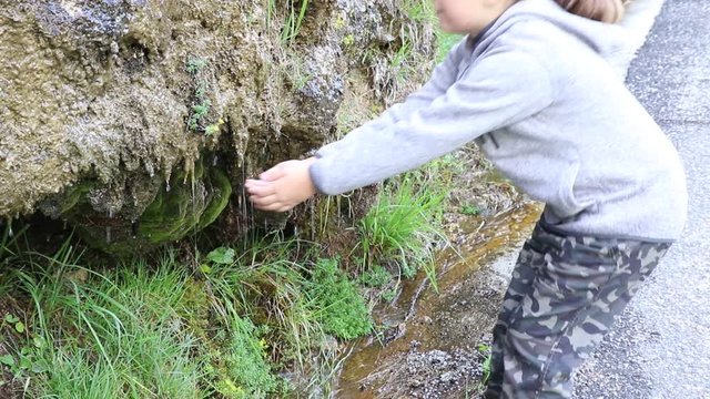 bambina beve dell'acqua fresca che esce dalla montagna