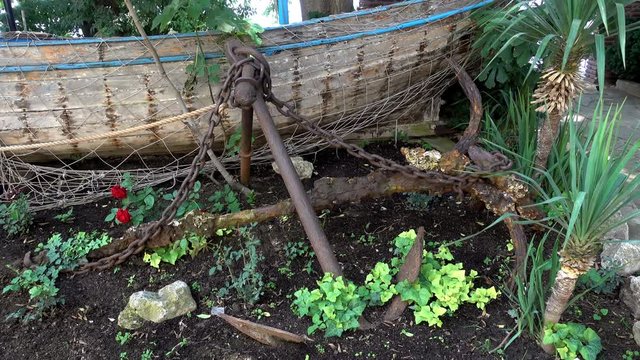4K view of decorative old anchor and boat on a flower bed.