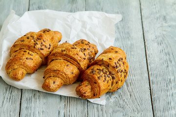 three delicious with croissant seeds lie diagonally in a row on white paper on a wooden background