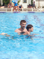Father is helping his son to obtain the swimming skills.