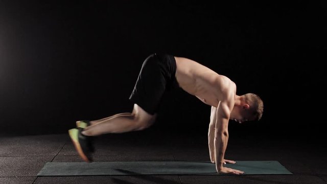 Sportsman doing plank with bunny hops on a mat in a professional studio.