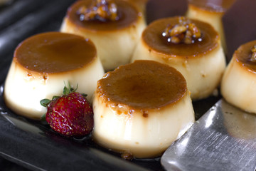 Traditional Turkish dessert - cream caramel, decorated with fresh strawberries, on a black tray