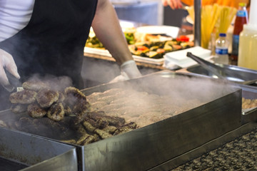 Cook's hand fries meat and burger cutlets on a steaming grill