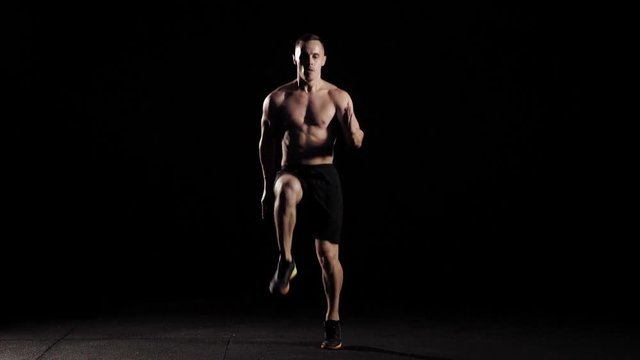 Young athlete with naked torso doing high knees running in place.